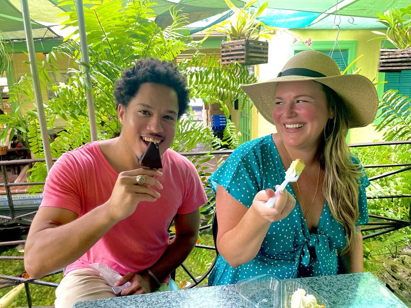 Two guests laughing over a chocolate-dipped Key lime pie on a stick at a leafy Key West patio