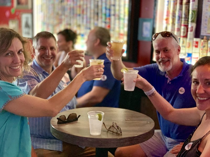 Tour group cheering with craft draft cocktails at Mary Ellen's, a Key West bar lined with vintage beer cans