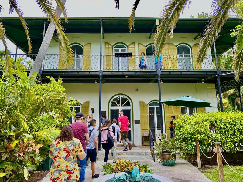 Tour group walking up to the Ernest Hemingway Home and Museum, with its yellow shutters and surrounding palms