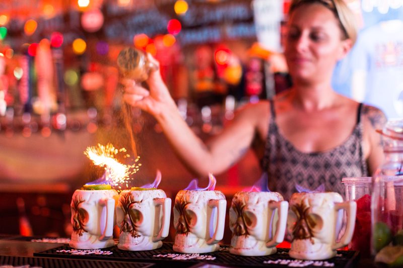 Bartender dusting cinnamon over a row of flaming tiki skull mugs at Tiki House in Key West