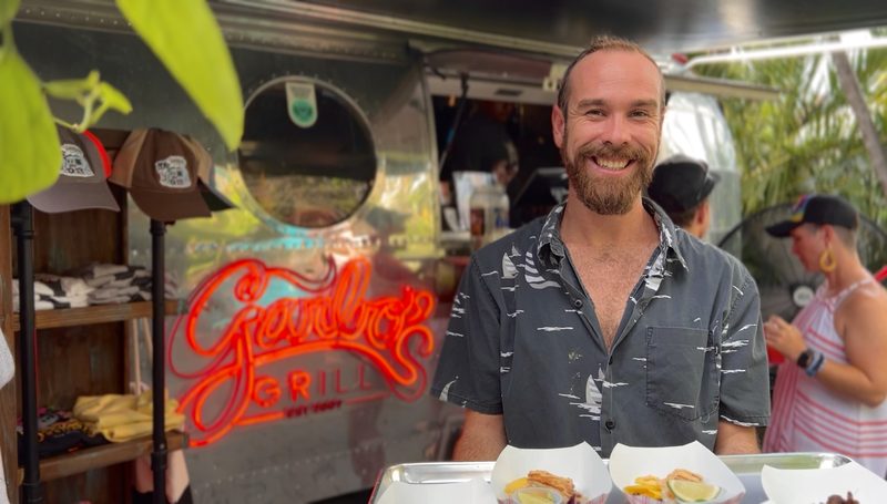 Guide carrying a tray of tastings in front of the neon-lit Garbo's Grill food truck in Key West