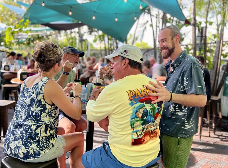 Guide chatting with seated tour guests under teal shade sails and string lights at Garbo's Grill and Hank's Saloon in Key West