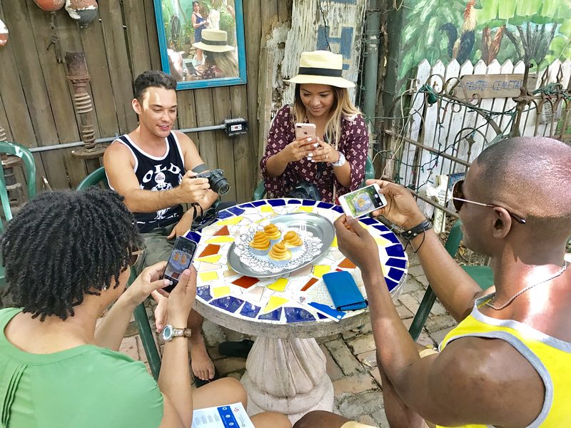 Tour guests photographing a plate of Cuban pastries on a mosaic tabletop in a Key West courtyard
