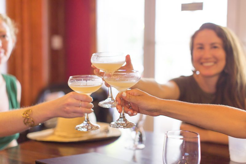 Three guests clinking coupe glasses in a toast at the Pilar Bar in The Saint Hotel, Key West