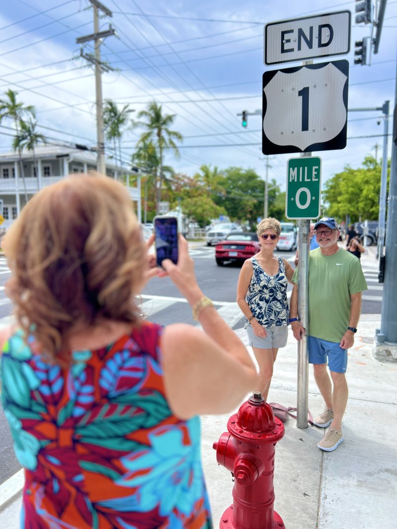 Tour guests posing for a photo at the Mile Marker 0 and End of US 1 signs in Key West