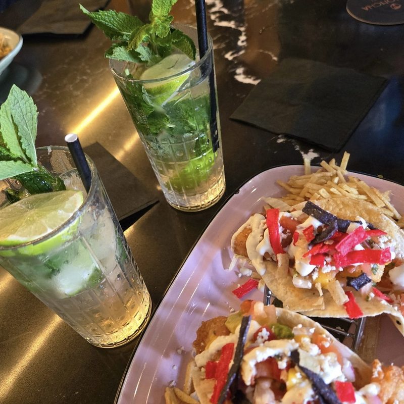 Two mint mojitos beside a plate of fish tacos topped with peppers and crema at the La Concha Hotel in Key West