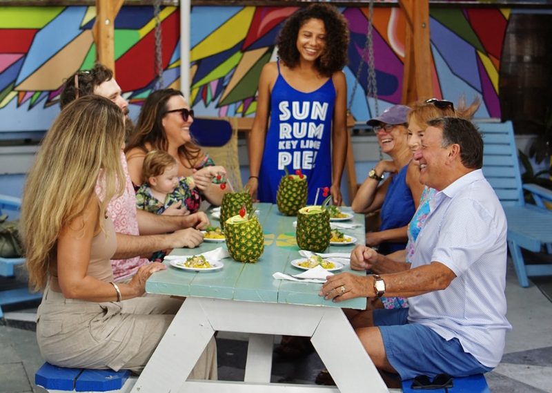 Tour group sharing tastings served in carved pineapples at a turquoise picnic table at Kaya's Backyard
