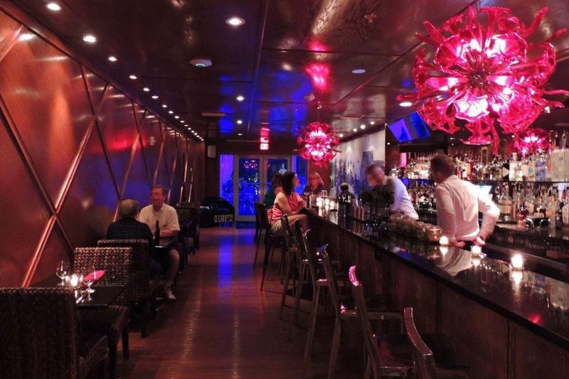 The dimly lit Pilar Bar at The Saint Hotel in Key West, with pink glass chandeliers above a long bar